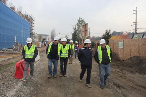 Un grupo de trabajadores de la construcción camina por un sitio de obra, todos con cascos y chalecos de seguridad.