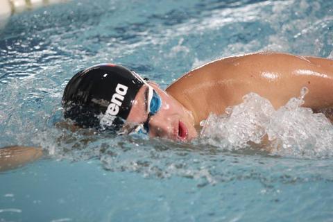 Un nadador compitiendo en una piscina, con un gorro y gafas de natación.