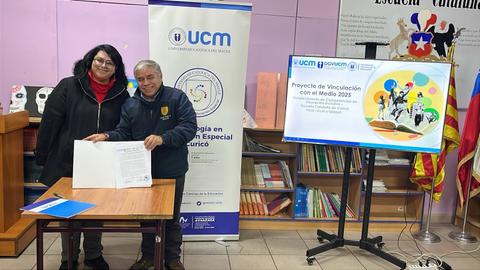 En la imagen se ve a dos personas firmando un acuerdo en una presentación en una escuela.