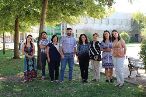 Un grupo de personas sonríe y se encuentra de pie en un parque con árboles al fondo.