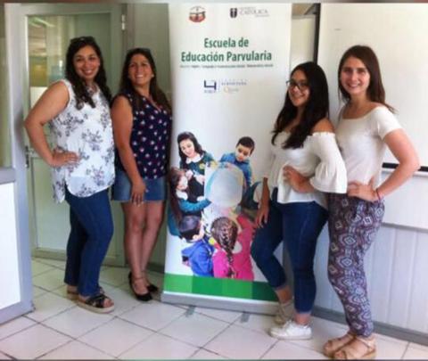 Cuatro mujeres posan frente a un banner de promoción de una escuela de educación parvularia.