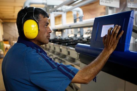 Un hombre con auriculares protectores interactúa con un panel de control en un entorno industrial.