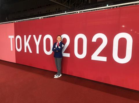 Una atleta sonríe junto a un gran cartel que dice 'TOKYO 2020'.