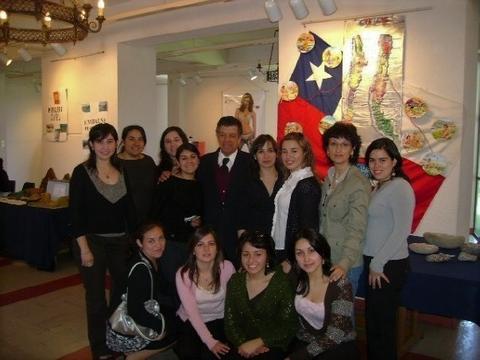 Un grupo de mujeres y un hombre posando juntos frente a una bandera chilena en un evento cultural.