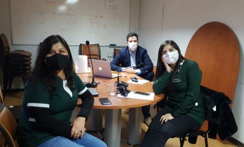 Un grupo de tres personas sentadas en una mesa de reuniones con computadoras y teléfonos móviles.