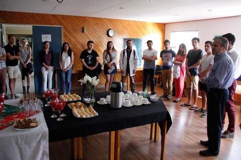 Un grupo de personas se encuentra reunido en una sala, observando un mesa con comida y bebidas.