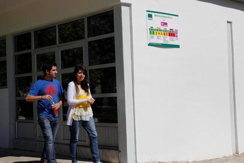 Una pareja camina frente a un edificio de paredes blancas con un cartel en la pared.