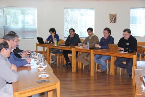 Un grupo de personas participan en una reunión en una sala con mesas de madera.