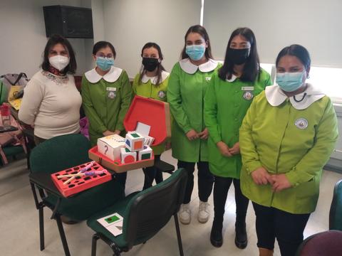 Un grupo de seis personas, con batas verdes y mascarillas, sonriendo en un aula.