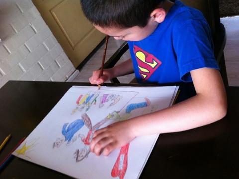 Un niño está dibujando en una hoja de papel mientras usa una camiseta azul con un logo en el pecho.