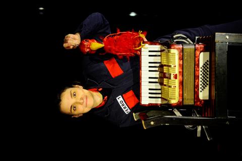 Una mujer sonriente sostiene un acordeón y un loro de peluche en un escenario.