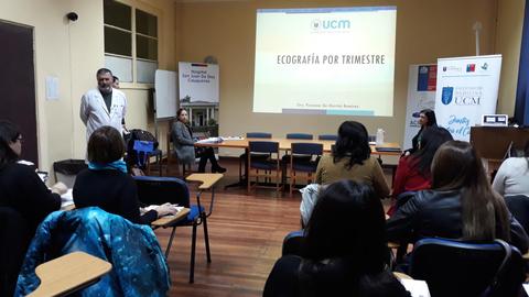 Una presentación sobre ecografía por trimestre en un aula con asistentes sentados.