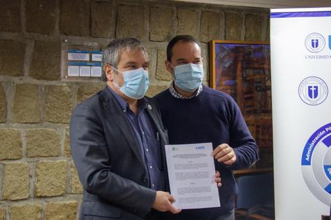 Dos hombres posan juntos sosteniendo un documento en un evento institucional.