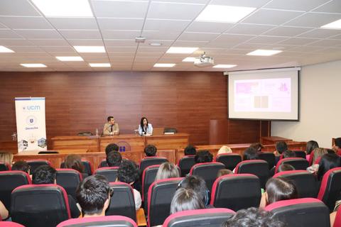 Un grupo de personas asiste a una conferencia en un auditorio con presentadores en el escenario.