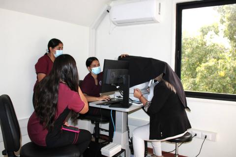 Cuatro personas en un ambiente de oficina, una de ellas usando un dispositivo conectado a un ordenador.