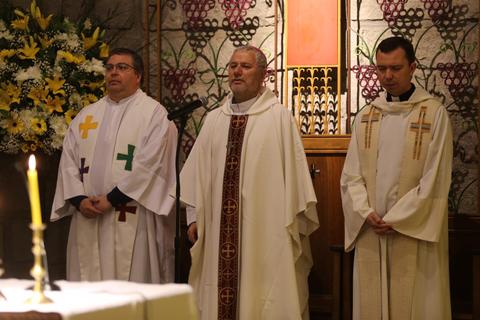 Tres sacerdotes en un altar durante una ceremonia religiosa.