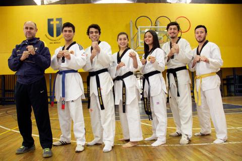 Un grupo de seis practicantes de taekwondo posan con sus cinturones en un gimnasio.