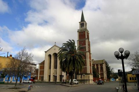 Iglesia con un campanario y una palmera en su entorno urbano.