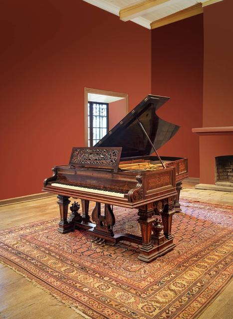 Un piano de cola de madera elegante situado en una habitación con paredes color rojo y un suelo de madera.