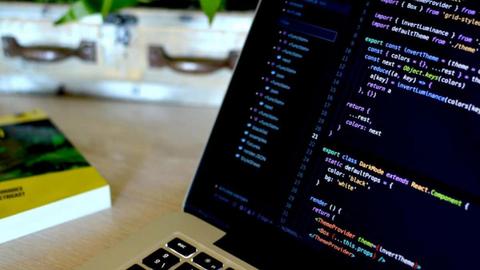 Un ordenador portátil mostrando código de programación sobre una mesa con un libro al lado.
