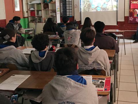 Un grupo de estudiantes sentado en un aula, mirando una presentación proyectada en una pantalla.