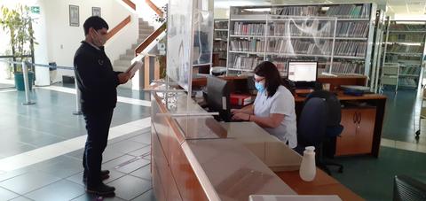 Un hombre está de pie frente a una mujer que trabaja en un escritorio en una biblioteca.