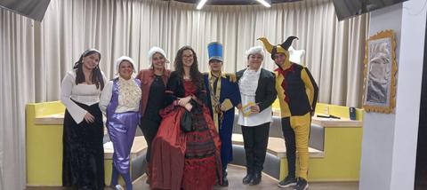 Un grupo de personas vestidas con trajes coloridos y diversos disfraces, posando juntas en un escenario interior.