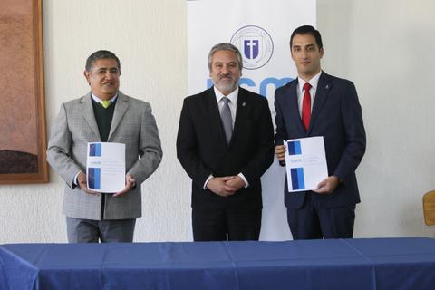 Tres hombres posan en un evento educativo sosteniendo documentos en un ambiente formal.