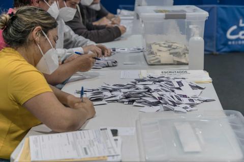Un grupo de personas se encuentra contando votos en una mesa electoral.