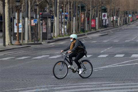 Una ciclista atraviesa una calle desierta con árboles y farolas.