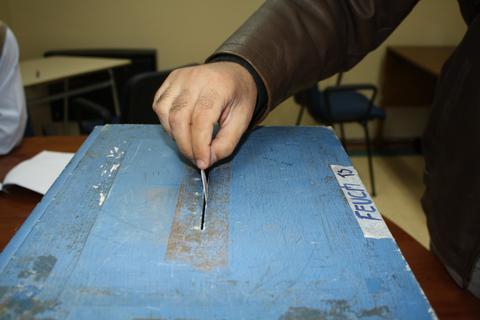 Una mano introduciendo una boleta en una urna electoral de color azul.