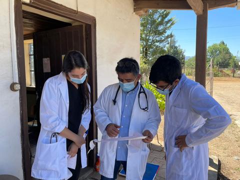 Tres personas con batas blancas revisan documentos en un entorno al aire libre.