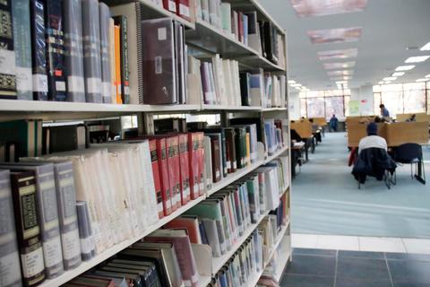 Una biblioteca con estanterías llenas de libros y personas leyendo en mesas cercanas.