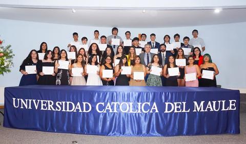 Una ceremonia de graduación con estudiantes sosteniendo certificados frente a un escenario decorado.