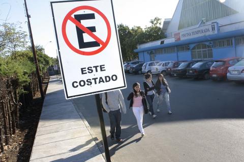 Un grupo de personas camina junto a un letrero que indica la prohibición de estacionar en ese costado.