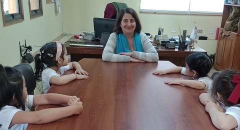 Una mujer sonriente se sienta frente a un grupo de niñas en una mesa.