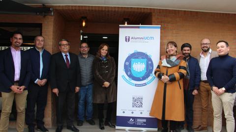 Un grupo de personas se reúne junto a un cartel de AlumniUCM en un evento.