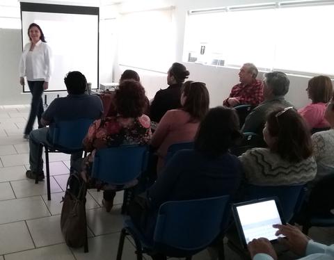 Una mujer presenta frente a un grupo de personas sentadas en un aula.