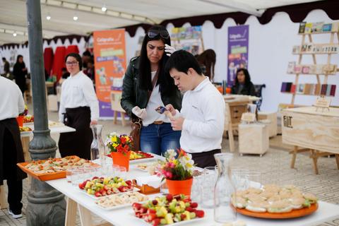 Una mujer y un niño observan una mesa llena de alimentos en un evento social.