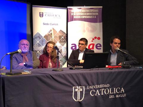 La imagen muestra a cuatro personas sentadas detrás de una mesa en un evento académico.