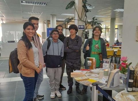 Grupo de jóvenes posando en un espacio de biblioteca con materiales de lectura.