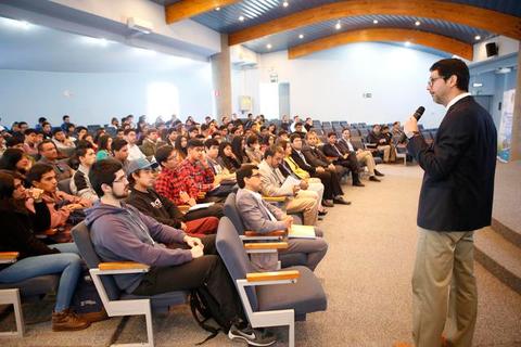 Un orador se dirige a una gran audiencia en un salón de conferencias.