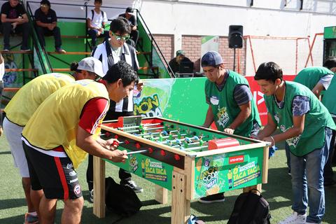 Un grupo de jóvenes compite en una mesa de futbolín en un evento recreativo al aire libre.