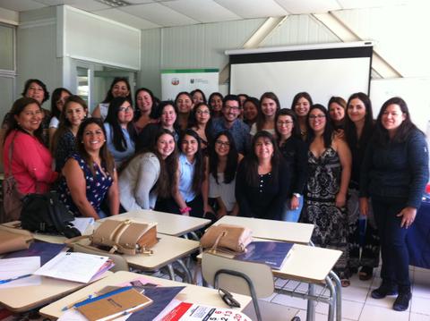 Un grupo grande de personas sonríen y posan juntas en un aula con proyector al fondo.
