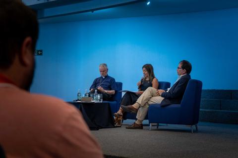 Tres personas sentadas en un escenario, participando en una conversación durante un evento.