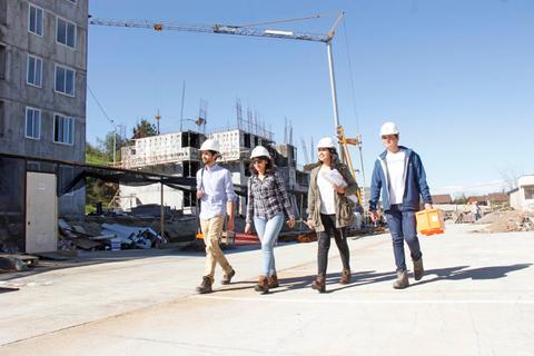 Un grupo de cuatro personas camina por un lugar de construcción bajo un cielo despejado.
