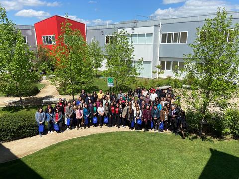 Una multitud de personas se agrupa en un amplio espacio verde frente a edificios modernos.