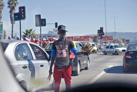 Un joven vende productos en la calle mientras los coches están detenidos en un semáforo.