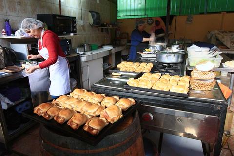 Una cocina con una mujer preparando alimentos y panes horneados en la mesa.