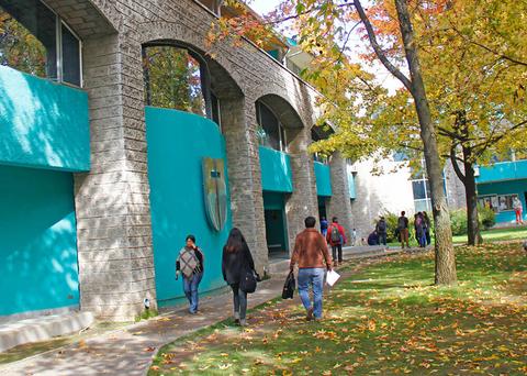 Una escena de un campus universitario con árboles y estudiantes caminando.
